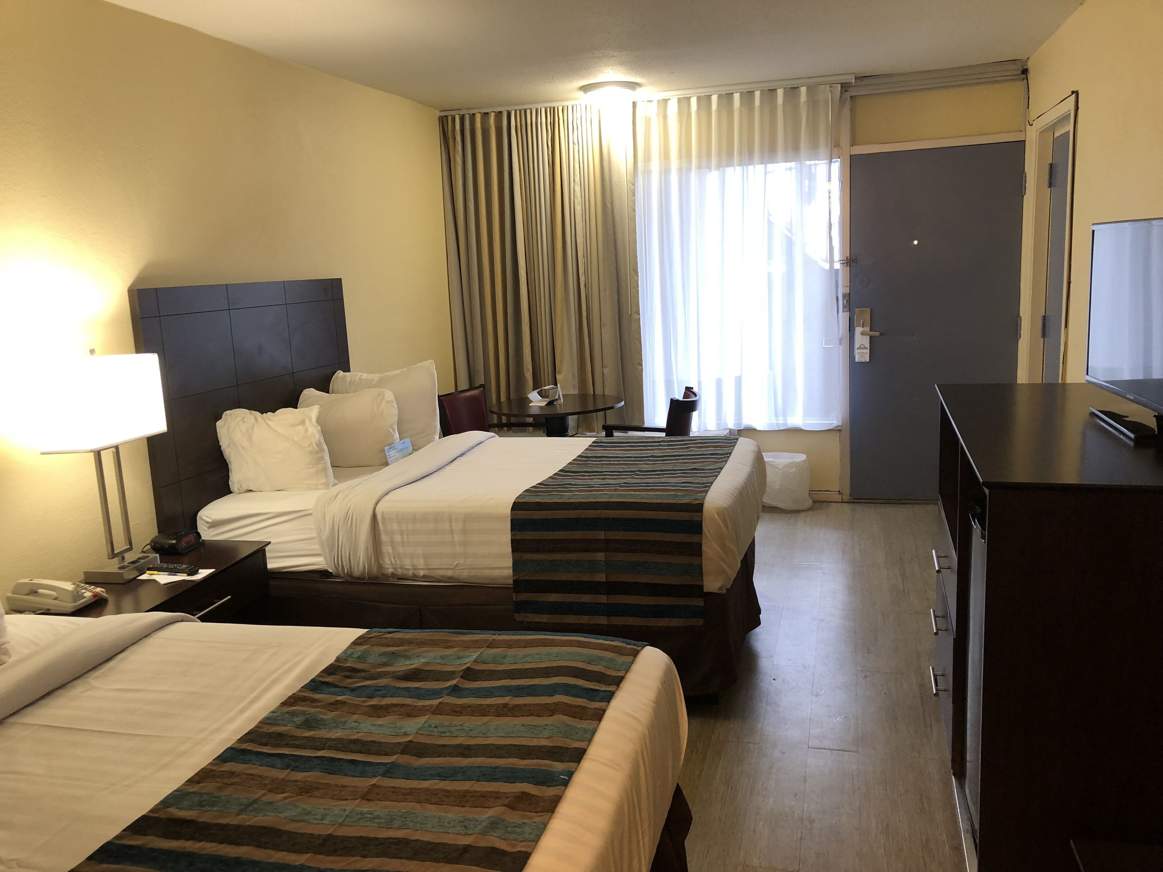 A hotel room with two beds, a desk, a chair, a television, and a window with curtains.