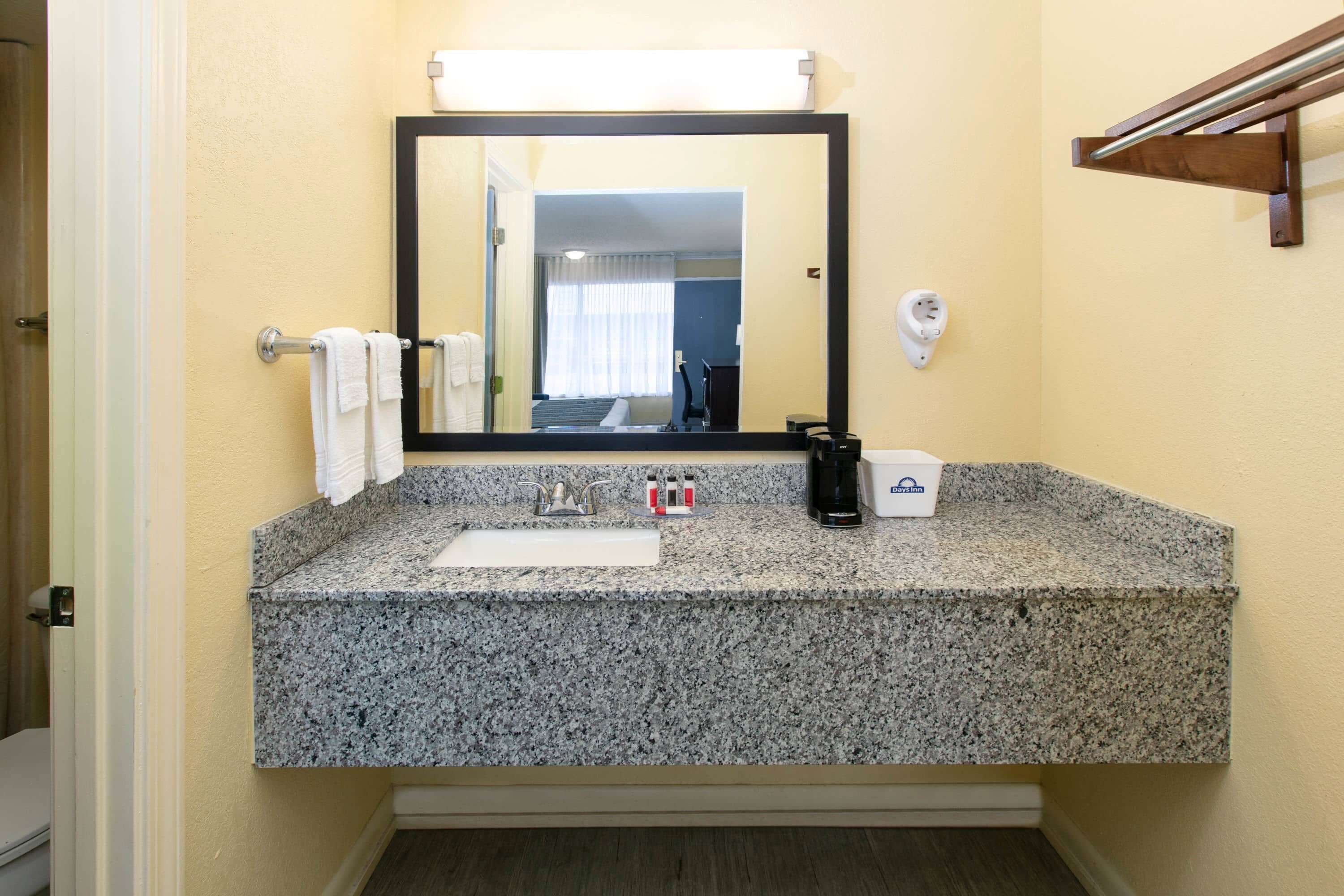 Une salle de bain avec un comptoir en granit, un lavabo, un miroir, un porte-serviettes et une machine à café.