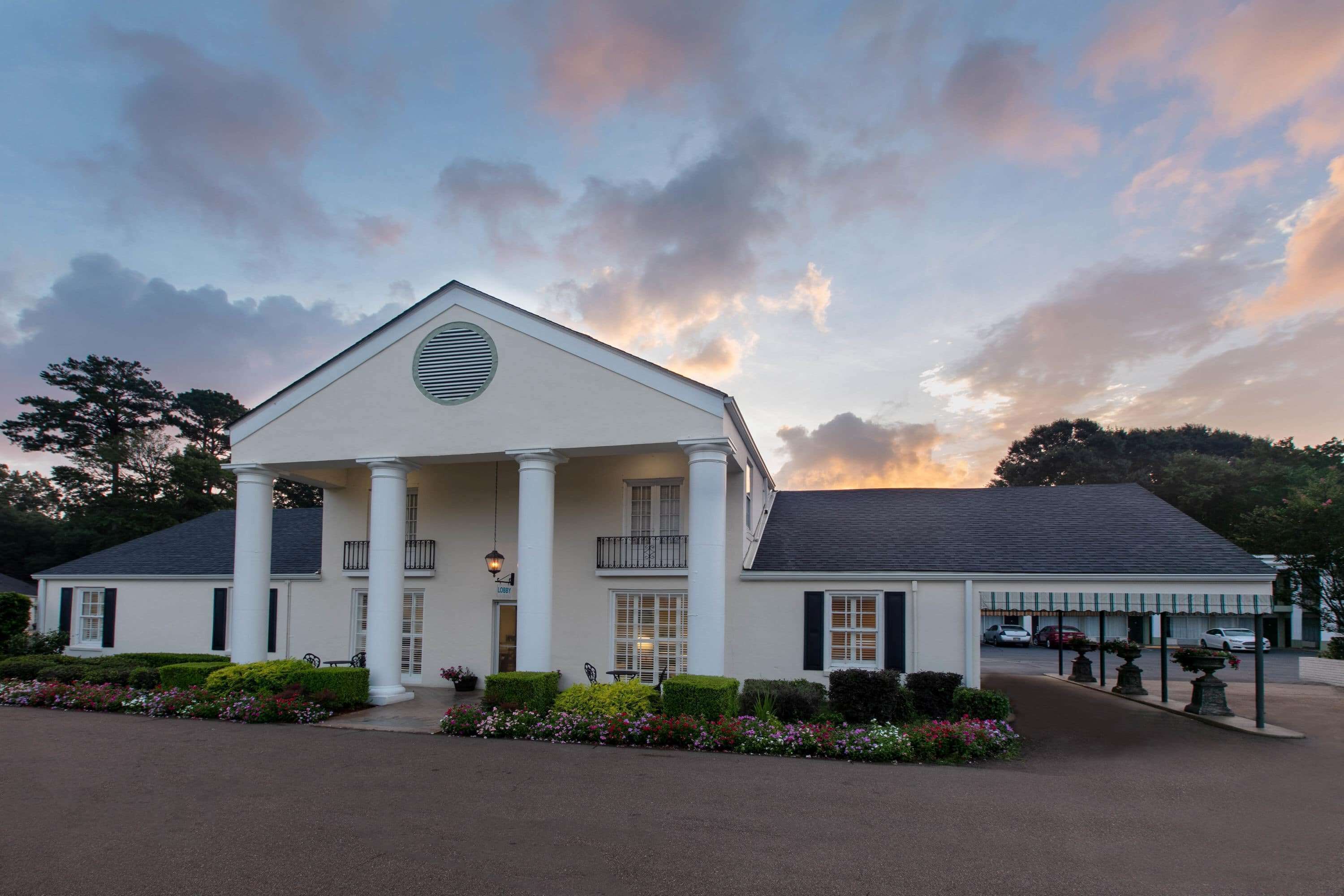 A white building with a central entrance, columns, and a covered porch area.