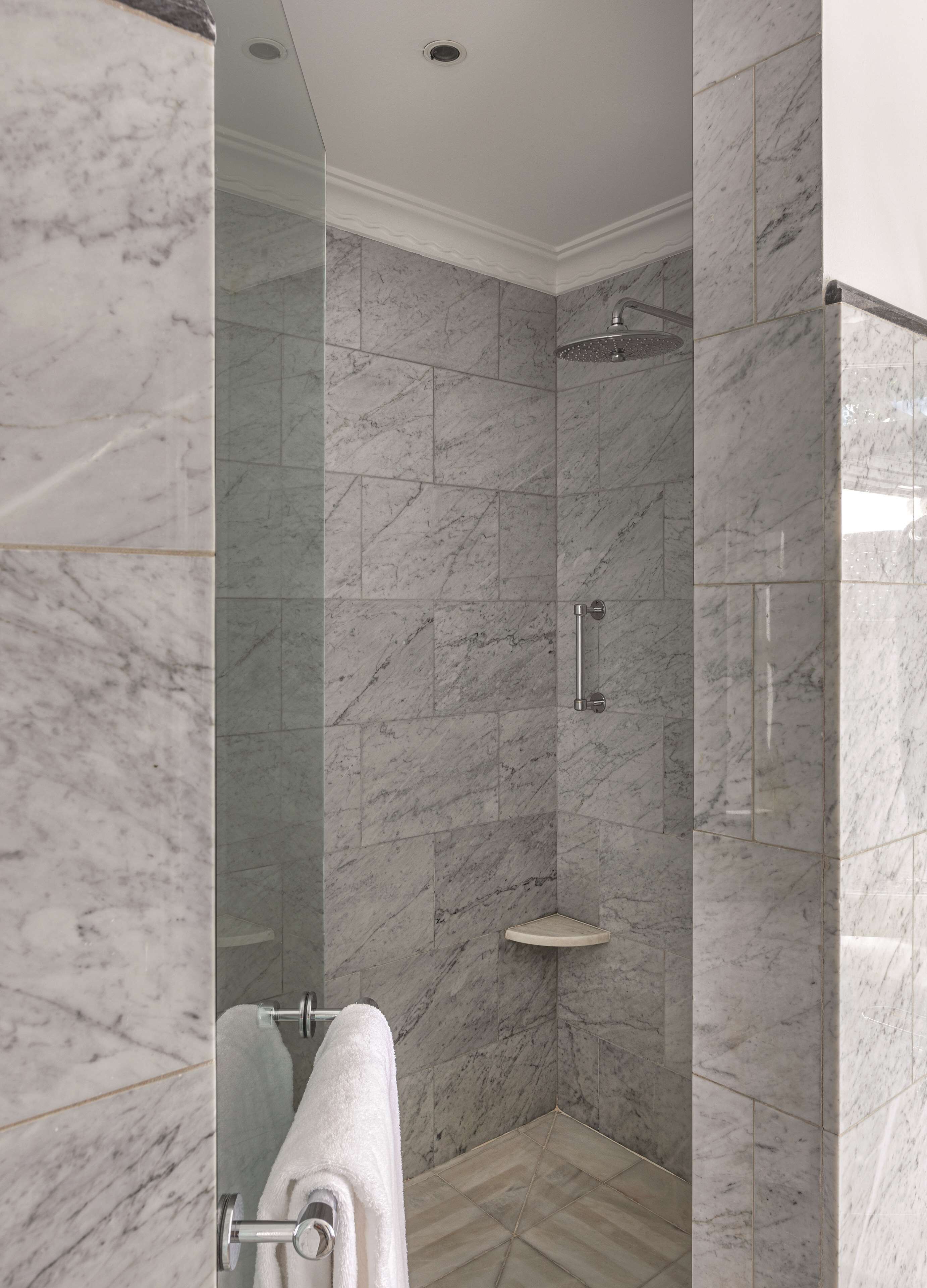 A modern bathroom with a glass-enclosed shower, marble walls, and a wooden floor.