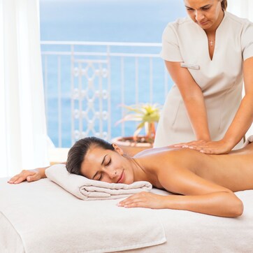 A massage therapy session in a room with a balcony overlooking the sea.