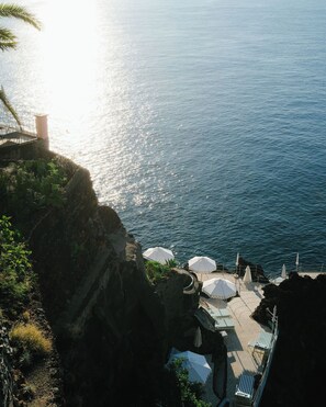 A coastal terrace with umbrellas and lounge chairs overlooking the sea. - Reid's Palace, A Belmond Hotel, Madeira (Funchal)