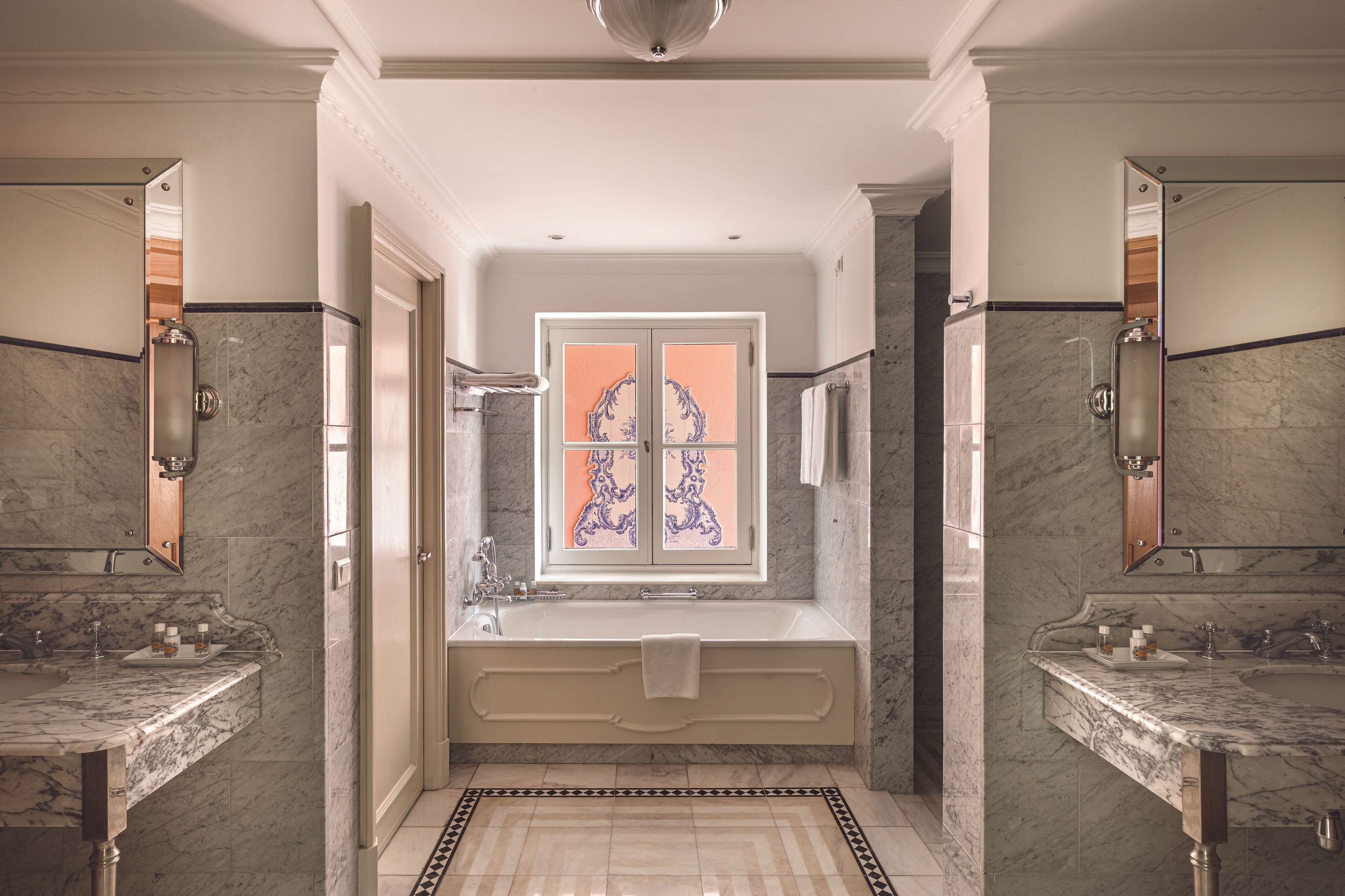 Um banheiro luxuoso com uma banheira grande, duas pias e uma janela decorativa com vitrais.