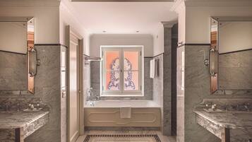 Um banheiro luxuoso com uma banheira grande, duas pias e uma janela decorativa com vitrais.