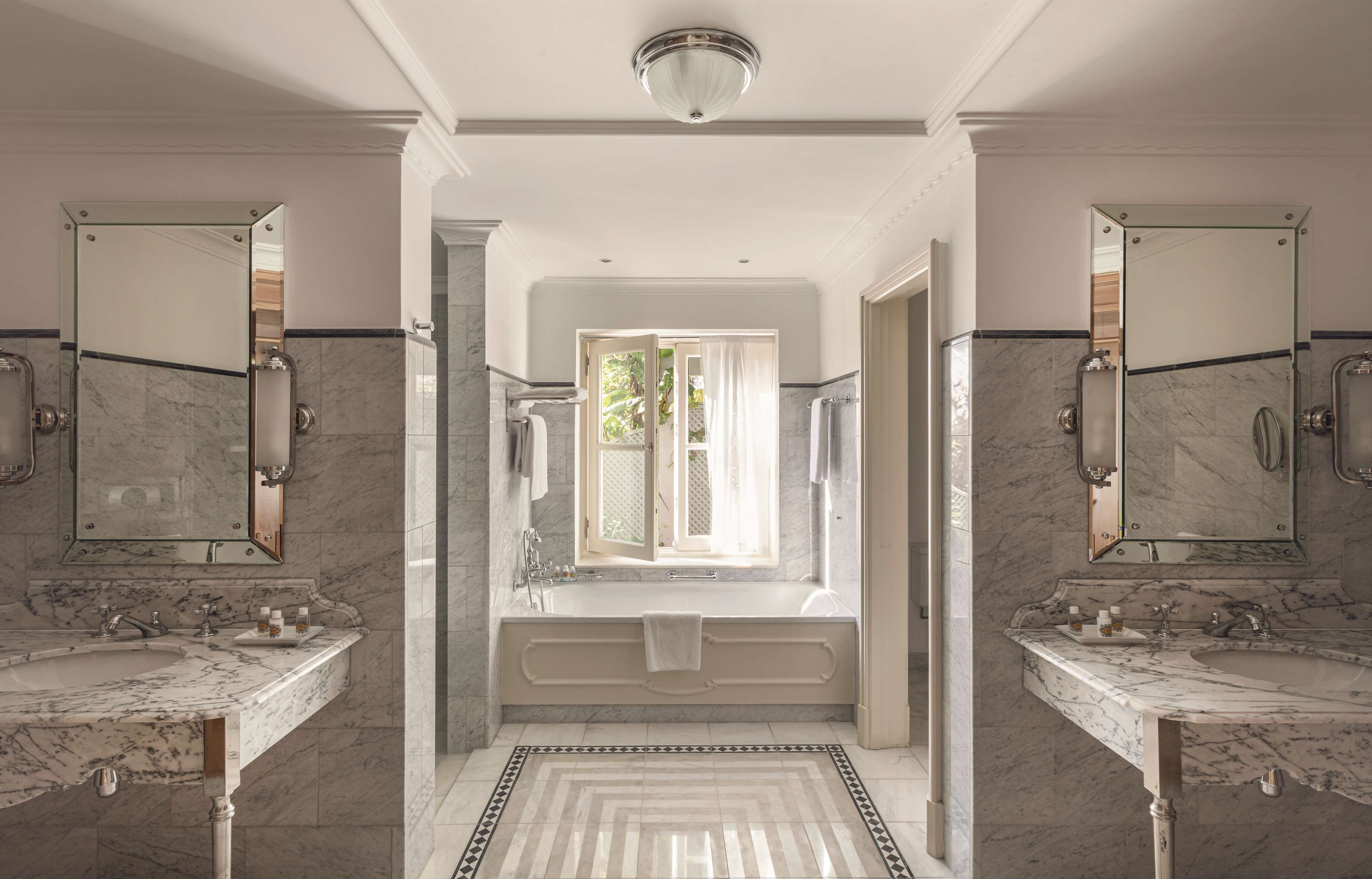 Une salle de bain luxueuse avec deux vasques en marbre, une grande baignoire et un miroir au-dessus de chaque vasque.