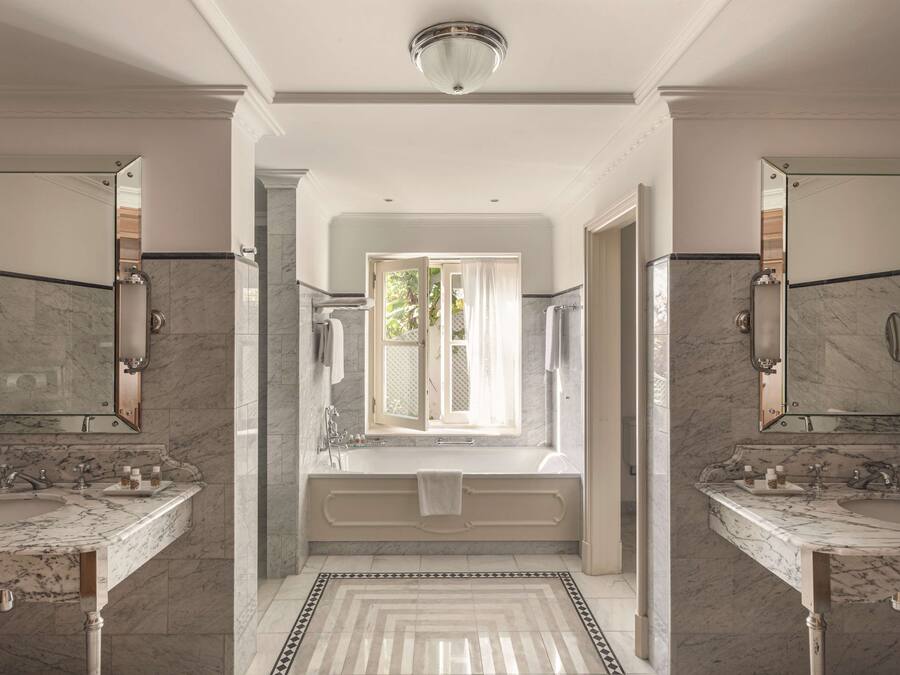 Une salle de bain luxueuse avec deux vasques en marbre, une grande baignoire et un miroir au-dessus de chaque vasque.