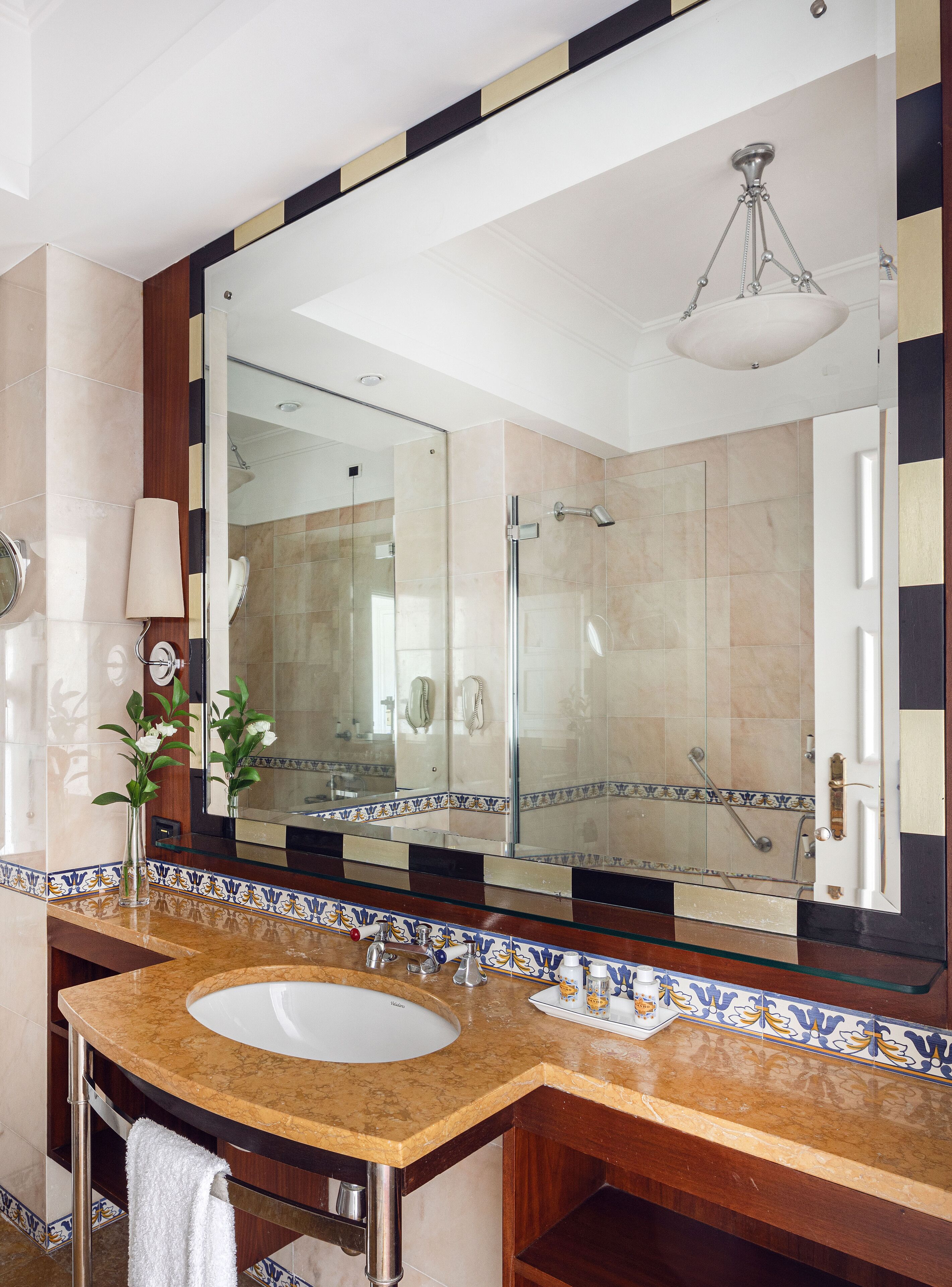A bathroom with a large mirror, a sink, a shower, and a towel rack.