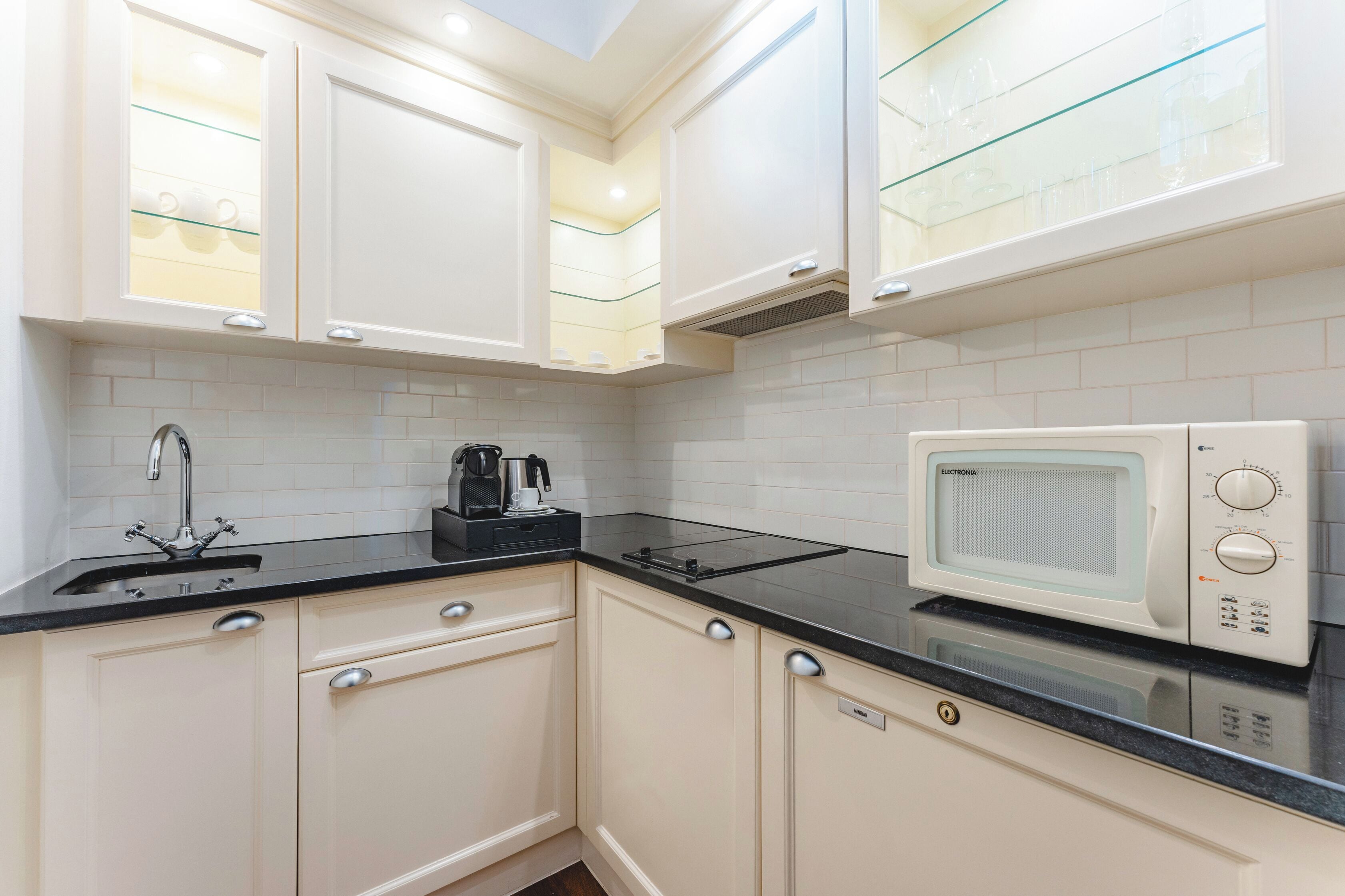 A kitchen with white cabinets, a black countertop, a coffee maker, and a microwave.