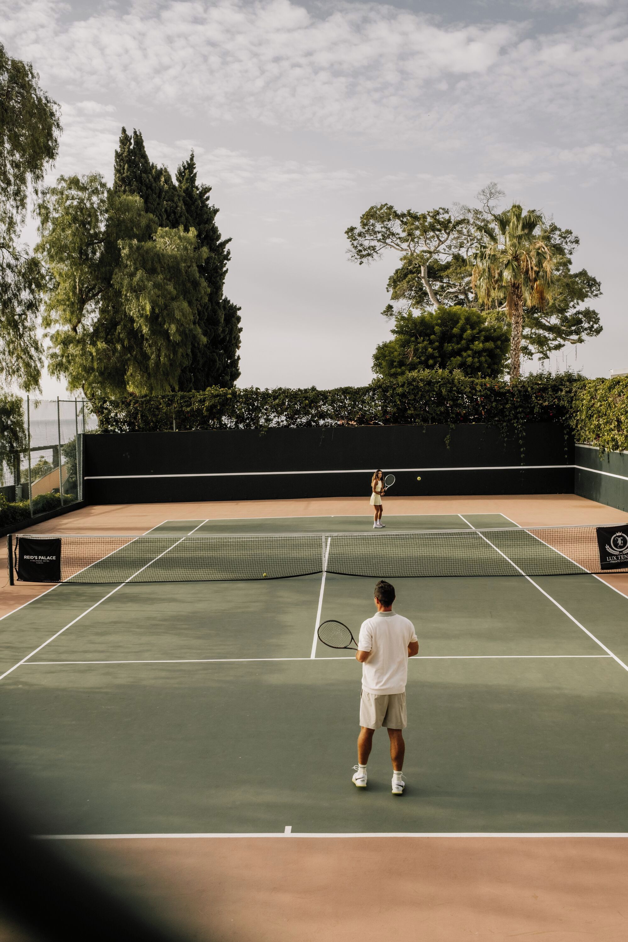 Ein Tennisplatz mit Netz, ein Spieler im Vordergrund und ein weiterer Spieler im Hintergrund.