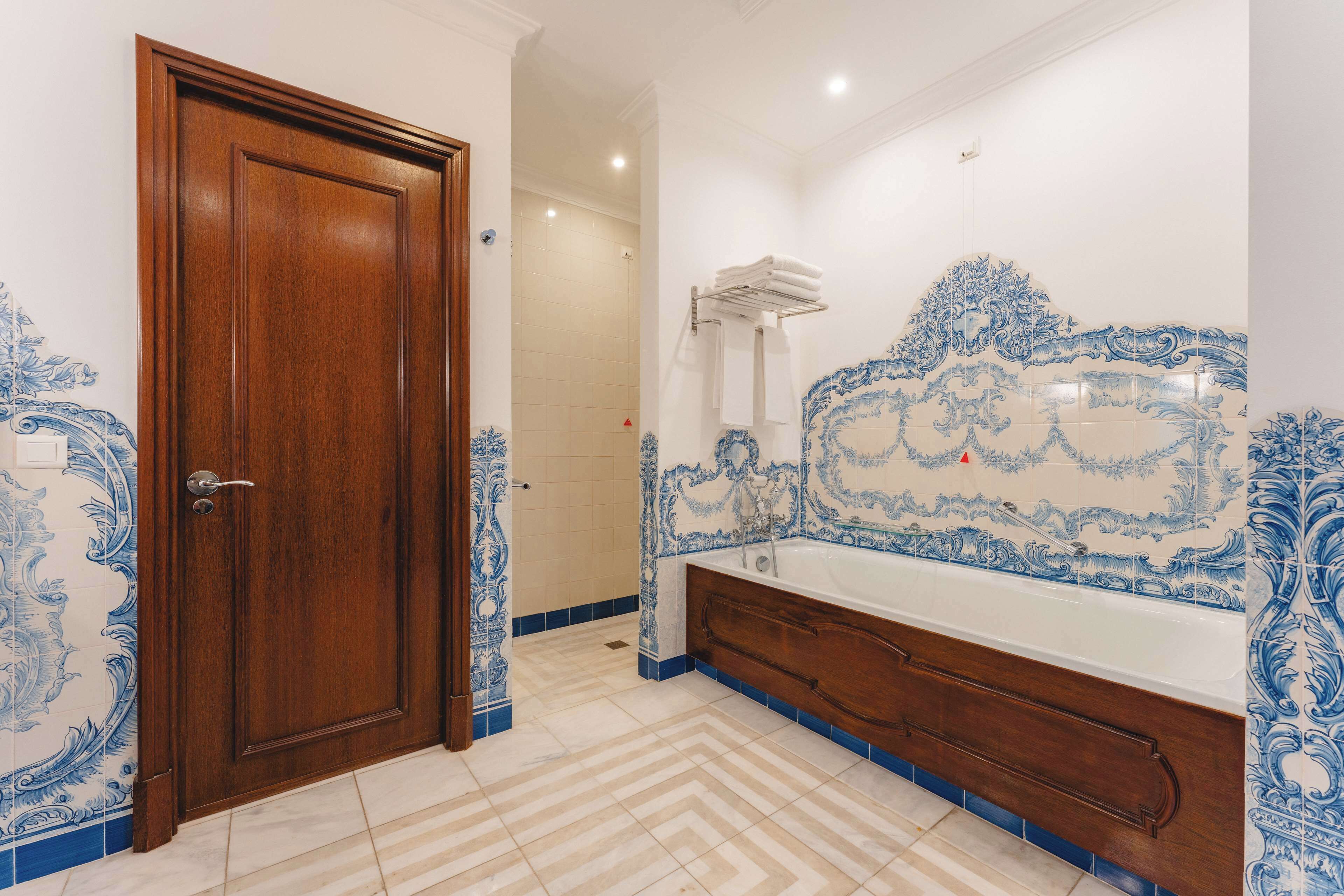 Un baño con puerta de madera, bañera con azulejos azules y blancos, y piso de baldosas.