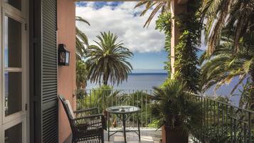 Een balkon met een tafel en stoelen, met uitzicht op een schilderachtig zeegezicht en palmbomen.