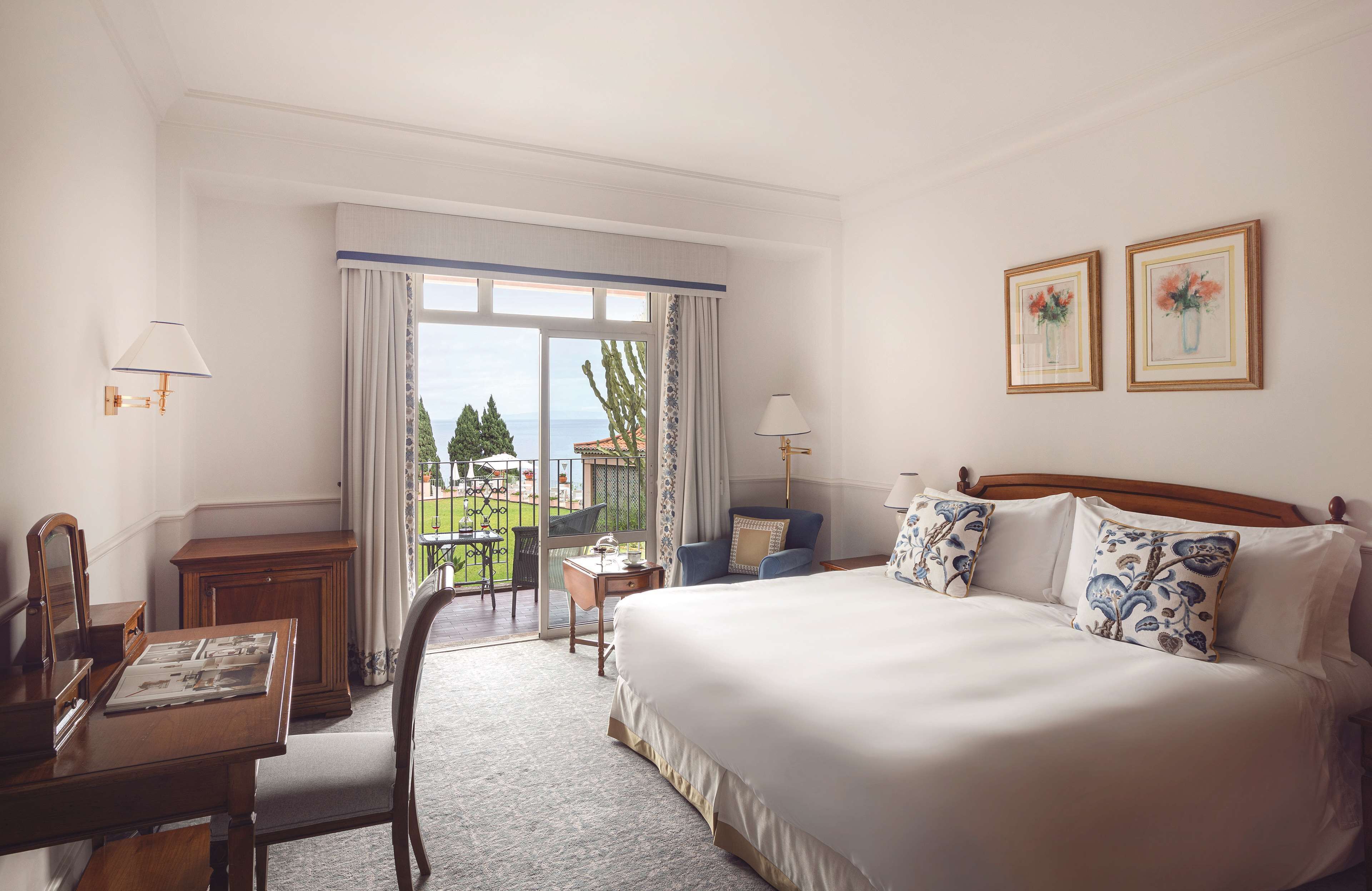 A hotel room with a large bed, a desk, a chair, and a balcony with a view.
