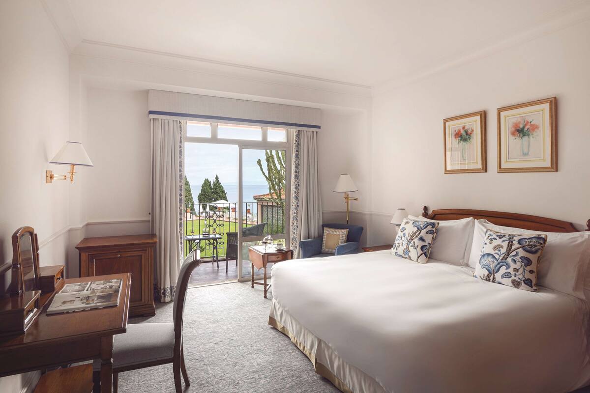 Een hotelkamer met een groot bed, een bureau, een stoel en een balkon met uitzicht.