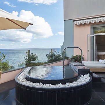 A hot tub with white pebbles, a lounge chair, and a view of the sea.