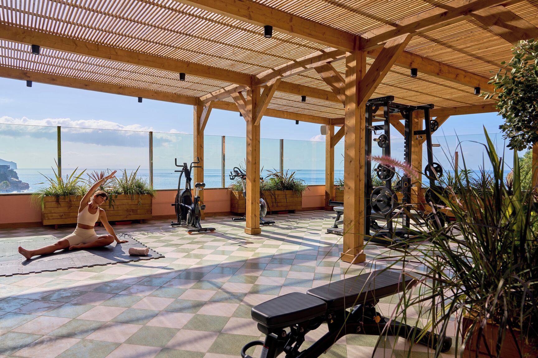 Un gimnasio con equipo de ejercicio, una colchoneta para yoga y vista al océano.