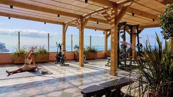 Un gimnasio con equipo de ejercicio, una colchoneta para yoga y vista al océano.
