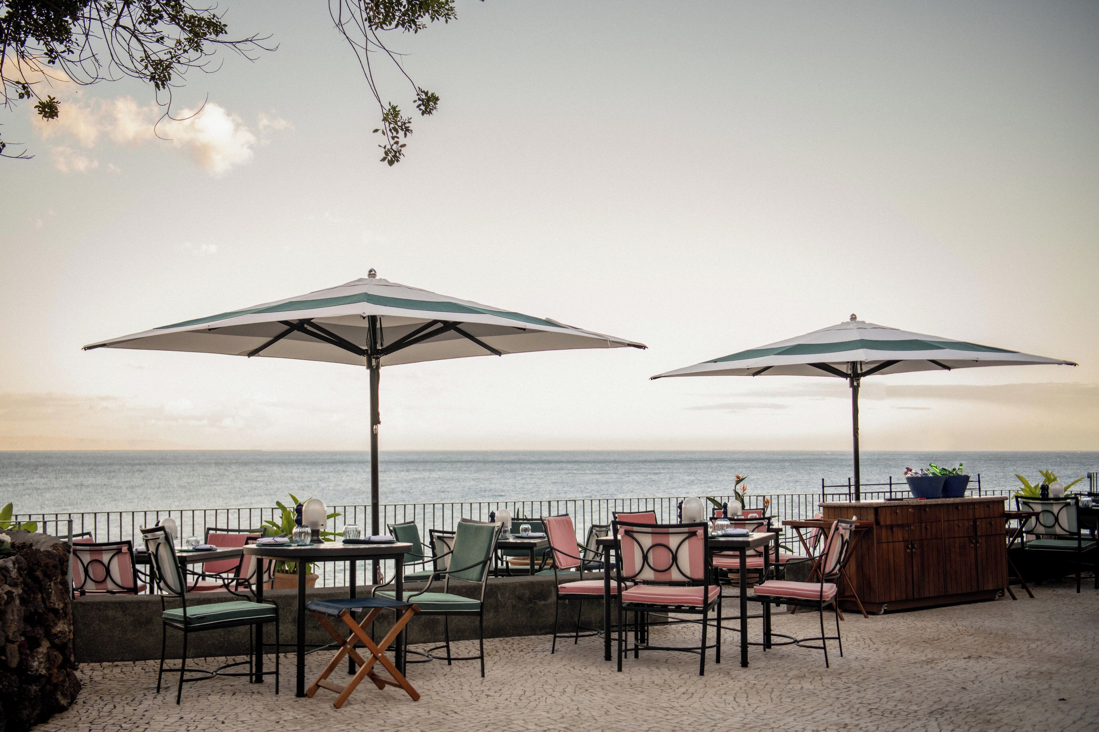 An outdoor seating area with tables and chairs, umbrellas, and a view of the sea.
