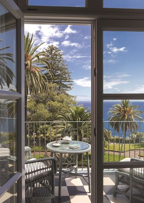 A balcony with a table and chairs, a view of the ocean, and tropical vegetation. - Reid's Palace, A Belmond Hotel, Madeira (Funchal)