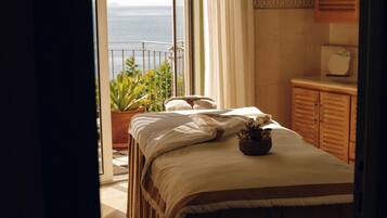 A bedroom with a bed, a potted plant, and a view of the sea through an open door.