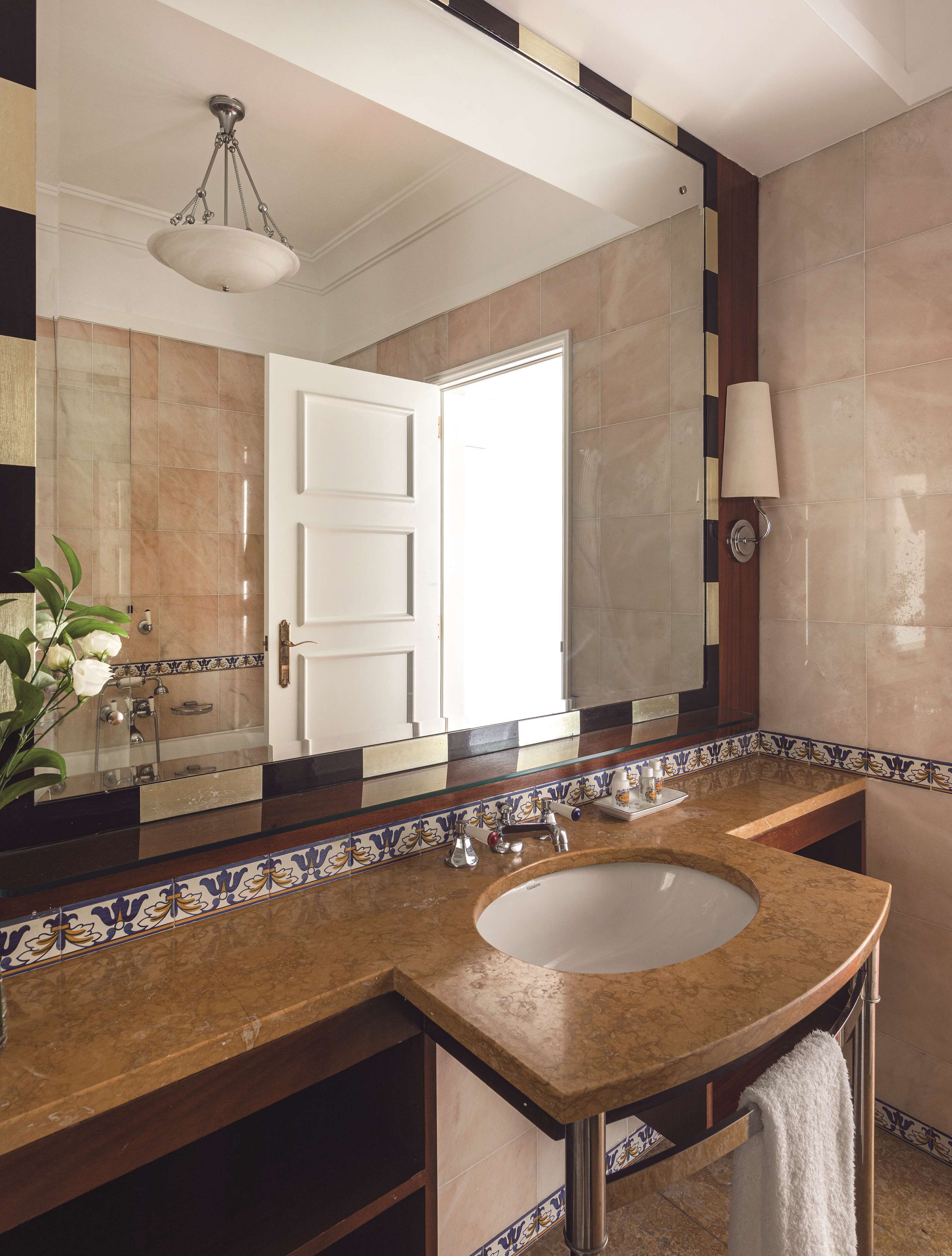 Une salle de bain avec un grand miroir, un lavabo, un porte-serviettes et une porte donnant sur une autre pièce.