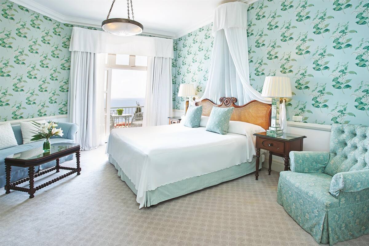 Een slaapkamer met een groot bed, een zithoek met een bank en een tafel, en een balkon met uitzicht.