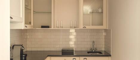 Cocina compacta con muebles blancos, encimera negra, pileta de acero inoxidable y luz empotrada en el techo.