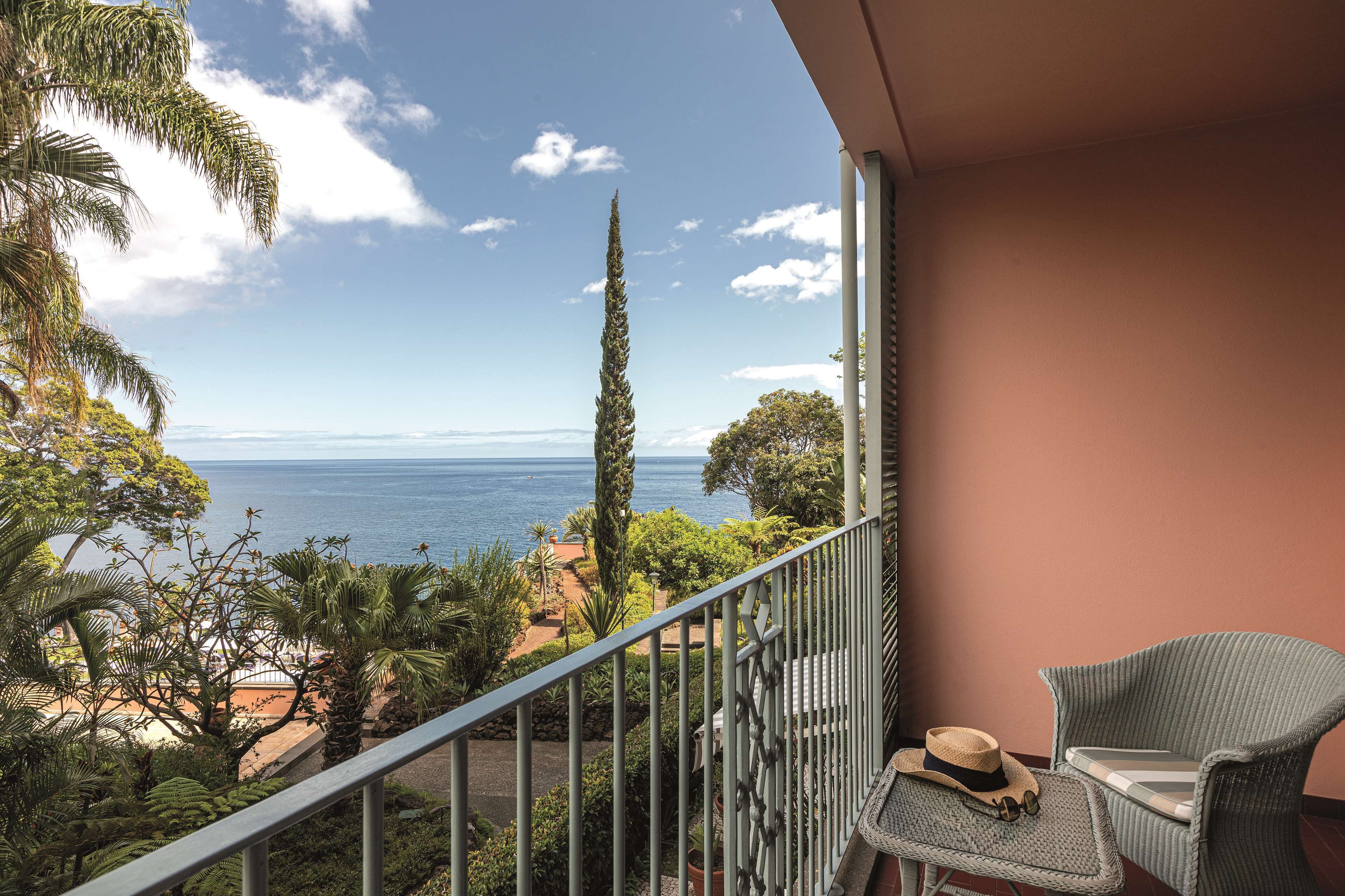 Ein Balkon mit Blick auf den Ozean, ein Korbstuhl, ein Hut und ein kleiner Tisch.