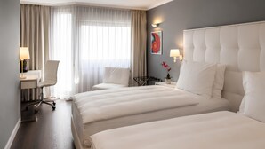 A hotel room with two beds, a desk, a chair, a window with curtains, and a wall-mounted artwork. - The Raphael Vienna Hotel, a member of Radisson Individuals Boutique (Vienna)
