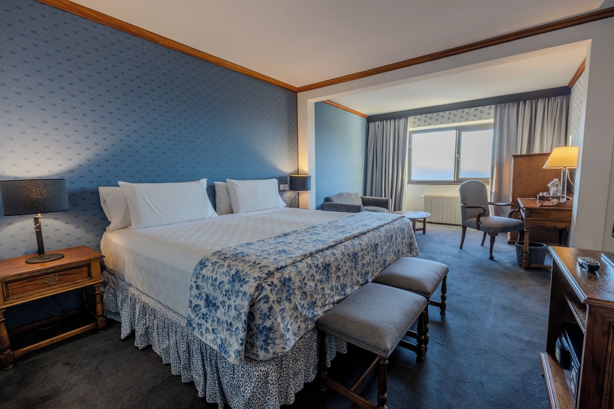 Une chambre d’hôtel avec un grand lit, un bureau, une chaise et une fenêtre avec des rideaux.