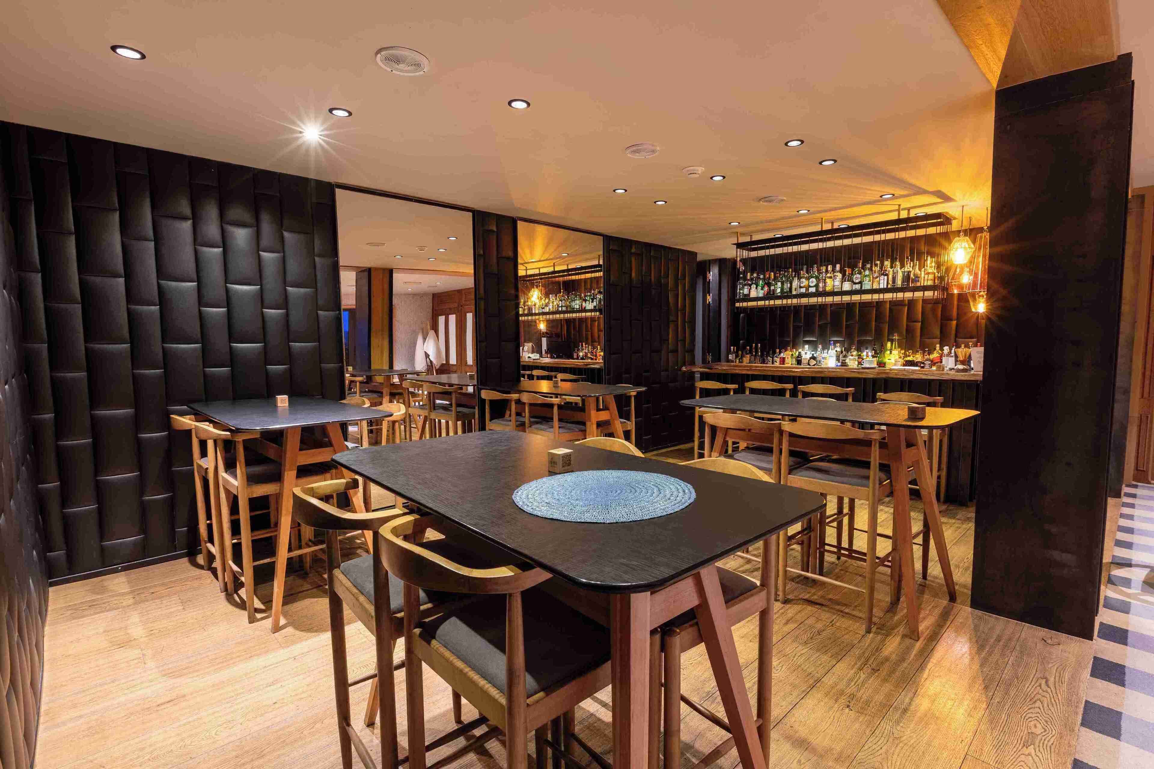 Een bar met verschillende tafels en stoelen, een toog vol flessen en een muur met een patroon.