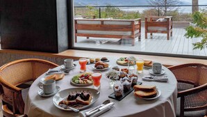 Een ontbijttafel met diverse gerechten, bergen zichtbaar door een groot raam, en houten meubels.
