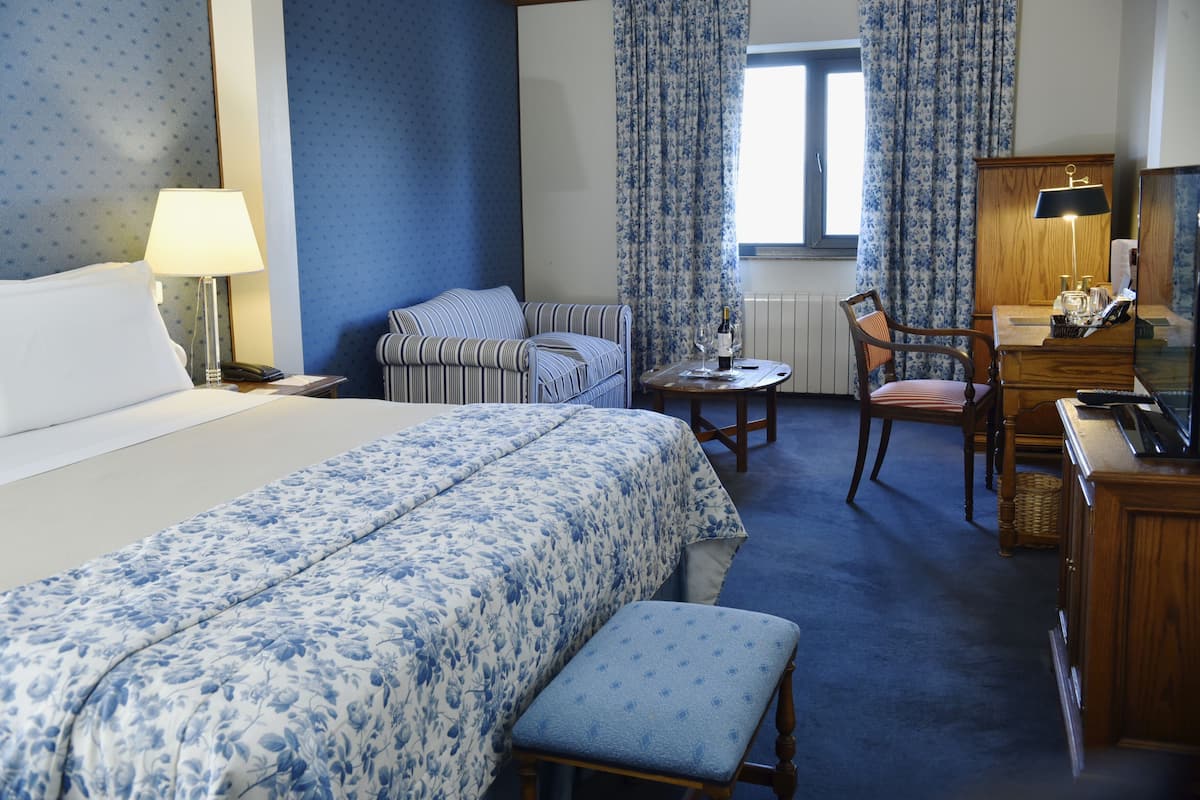 Une chambre d’hôtel avec un lit, un bureau, une chaise, une petite table et une lampe.