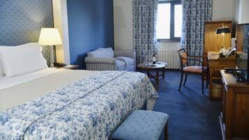 Une chambre d’hôtel avec un lit, un bureau, une chaise, une petite table et une lampe.