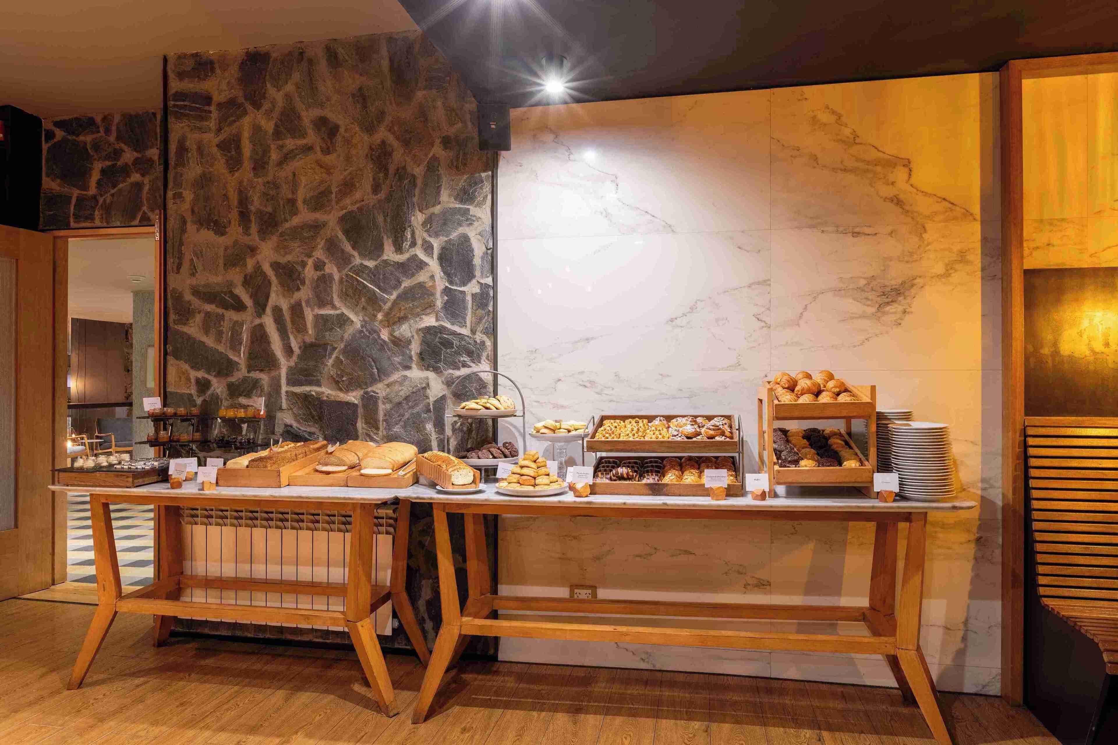Un buffet de petit-déjeuner proposant une variété de viennoiseries et de pains, le tout dans un cadre constitué de murs en pierre et en marbre.