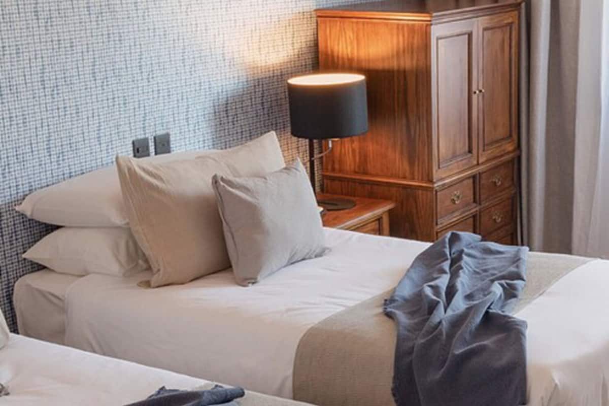 Une chambre d’hôtel avec un lit, une table de chevet, une lampe et une armoire en bois.