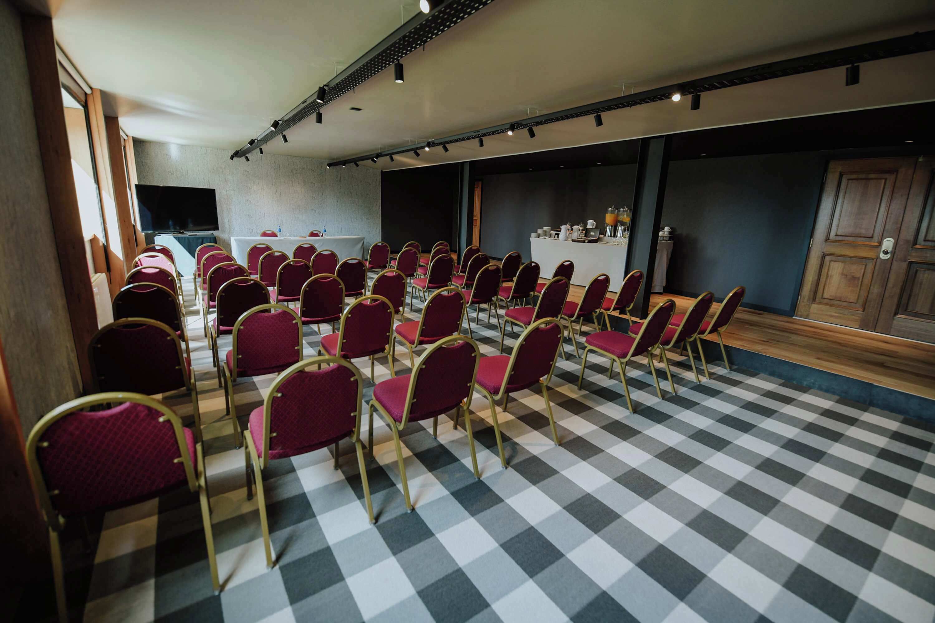 A conference room with rows of red chairs, a large table, and a flat-screen TV.