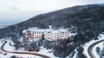 A large building with multiple wings, surrounded by snow-covered trees and a winding road.