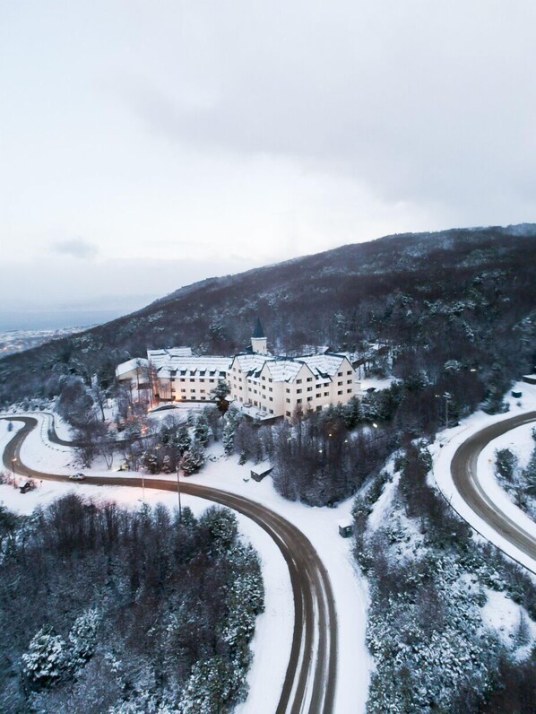 A large, multi-story building with a central tower, surrounded by snow-covered trees and a winding road.