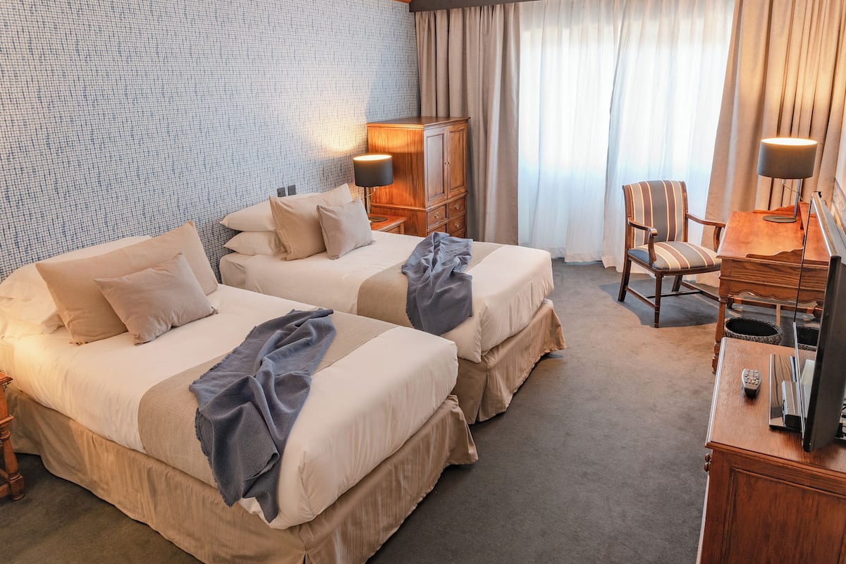 Une chambre d’hôtel avec deux lits, un bureau, une chaise, une armoire et une lampe.