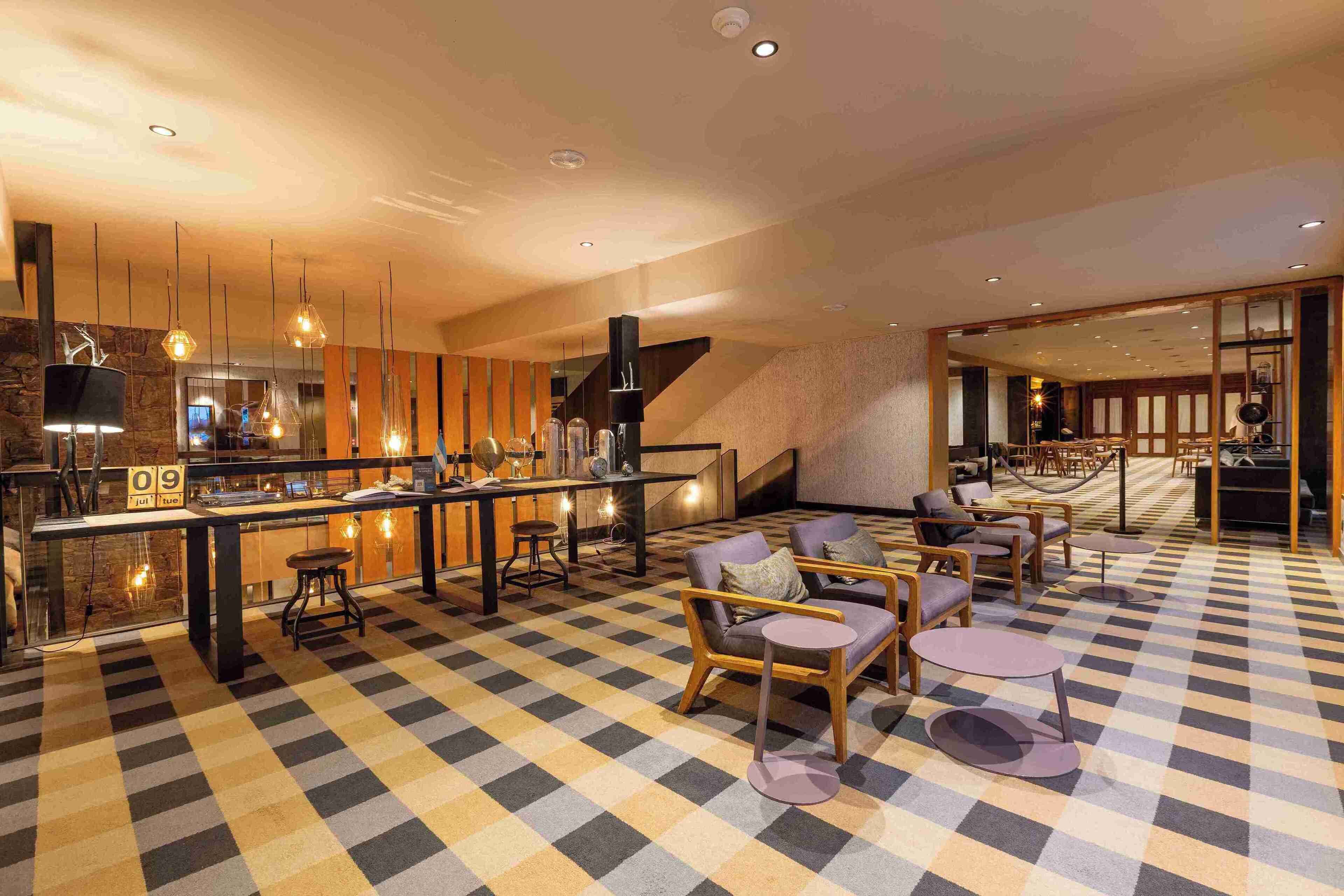 Un moderno vestíbulo de hotel con piso a cuadros, zona de estar, bar y una escalera.