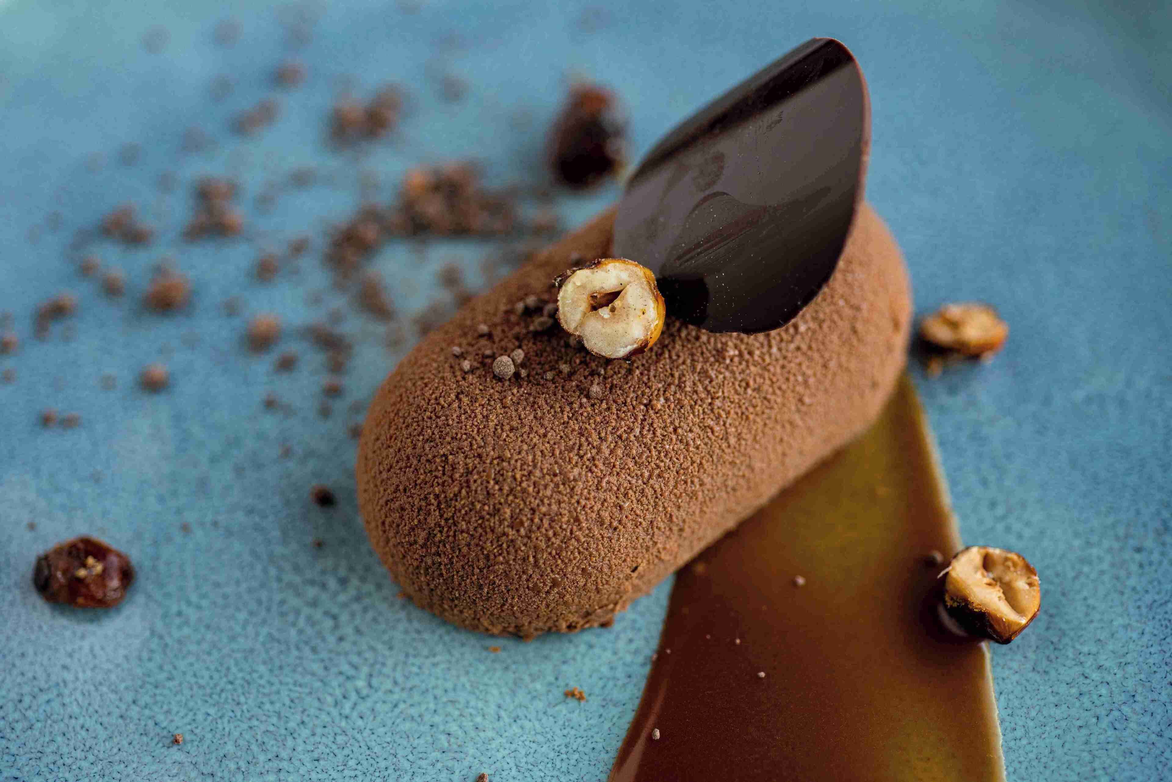 Un postre con chocolate y nueces sobre una superficie azul con textura.