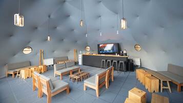 A modern lounge area with sofas, tables, and bar stools, featuring a tufted ceiling and pendant lighting.