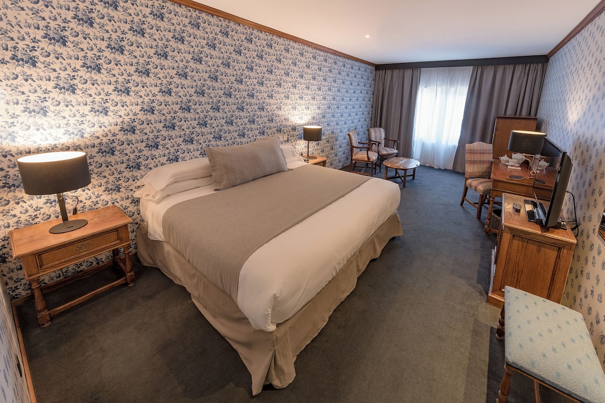 Une chambre d’hôtel avec un grand lit, deux tables de chevet avec des lampes, un bureau avec une chaise et une petite table avec une chaise.