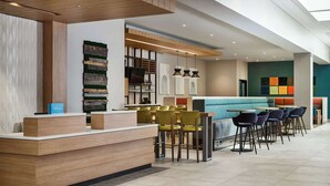 A modern hotel lobby with a reception desk, seating area, and decorative wall panels. - Hilton Garden Inn Tewksbury Andover (Tewksbury)