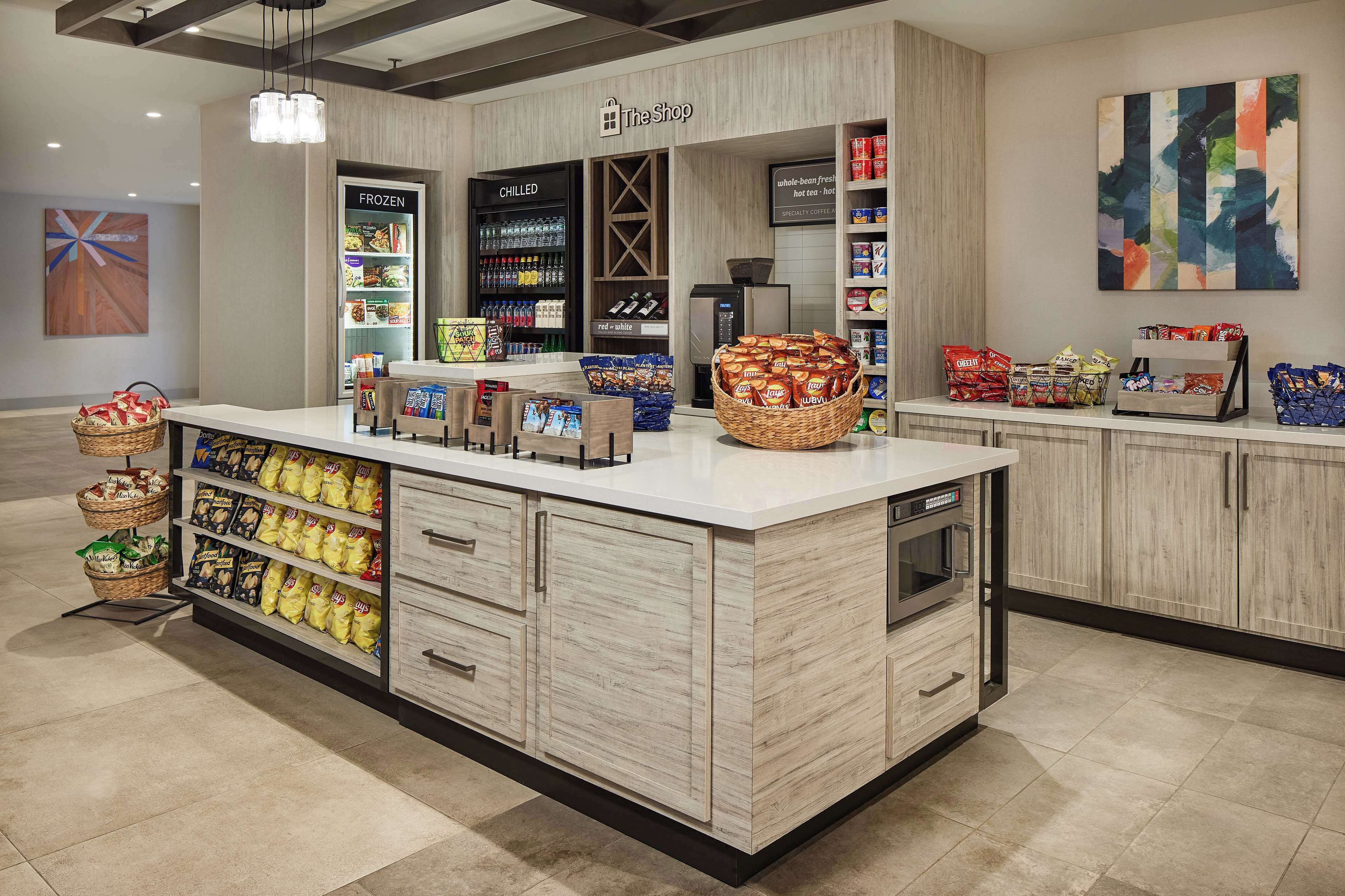 A clean, modern grocery store interior with a central island stocked with snacks, a refrigerated section, and a variety of packaged goods on shelves.