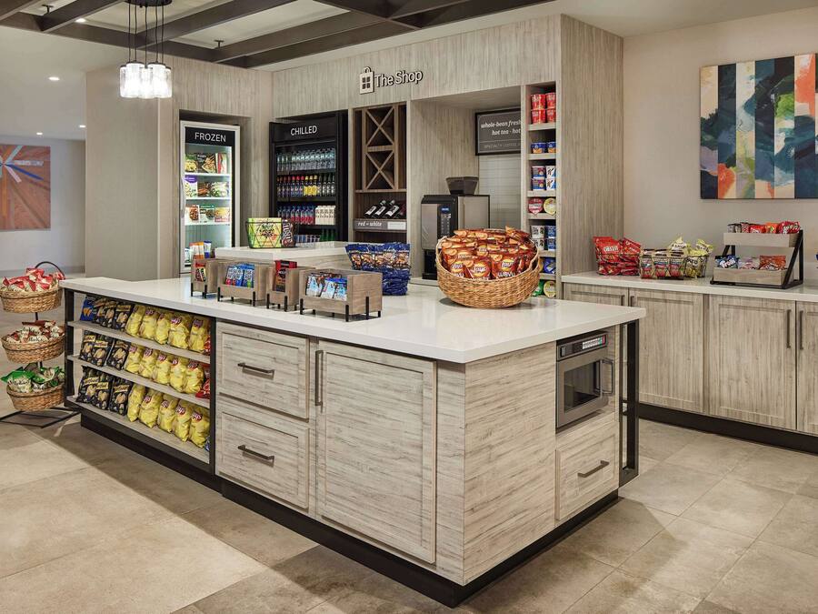 Interior de um supermercado limpo e moderno, com uma ilha central repleta de lanches, uma área refrigerada e diversas embalagens em prateleiras.