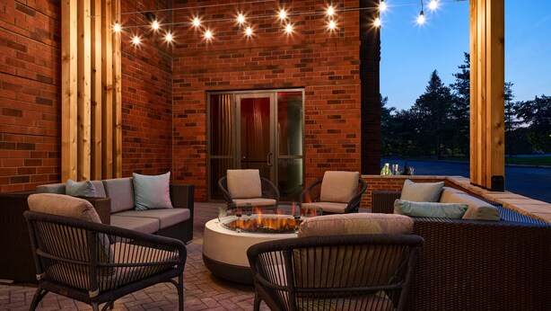 An outdoor patio area with wicker furniture, a fire pit, and string lights. - Hilton Garden Inn Tewksbury Andover (Tewksbury)