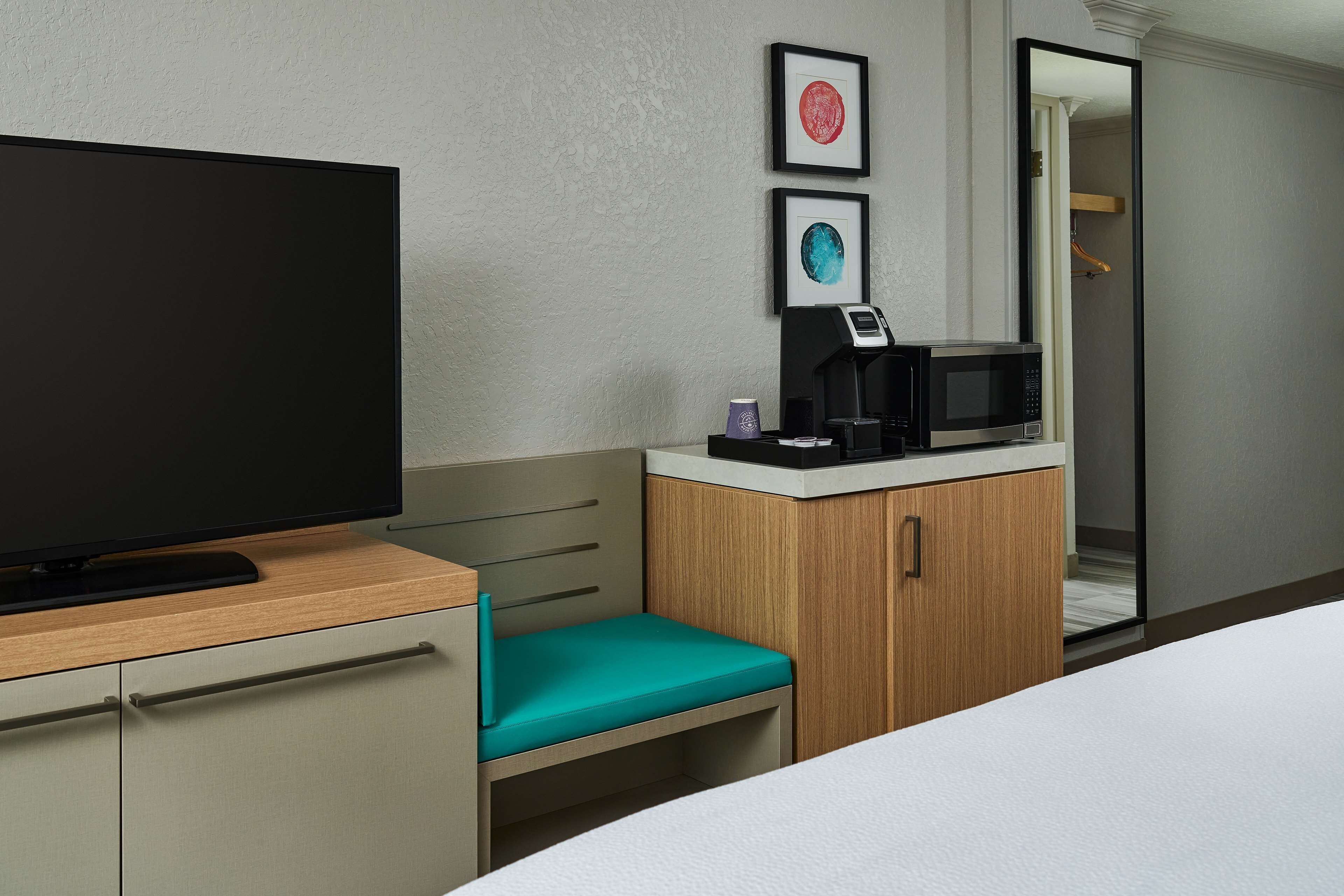 A hotel room with a television, a microwave, a small table with a coffee maker, and a teal chair.