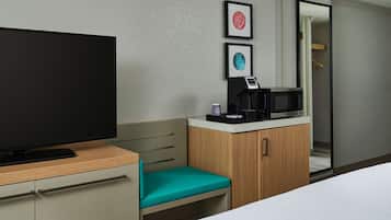 A hotel room with a television, a microwave, a small table with a coffee maker, and a teal chair.