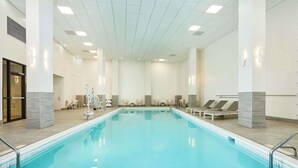An indoor swimming pool with clear water, surrounded by lounge chairs and a tiled floor. - Hilton Garden Inn Tewksbury Andover (Tewksbury)